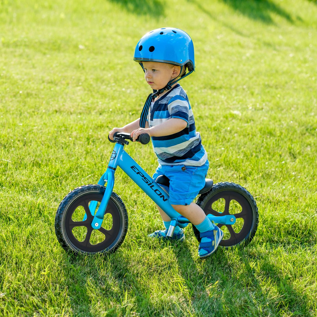 Young child riding a blue Epsilon children's balance bike on grass