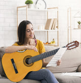 Woman sitting on a couch playing an acoustic guitar while reading sheet music